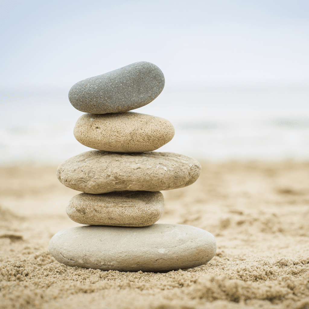 Stacked smooth stones on a sandy beach with a blurred sea background