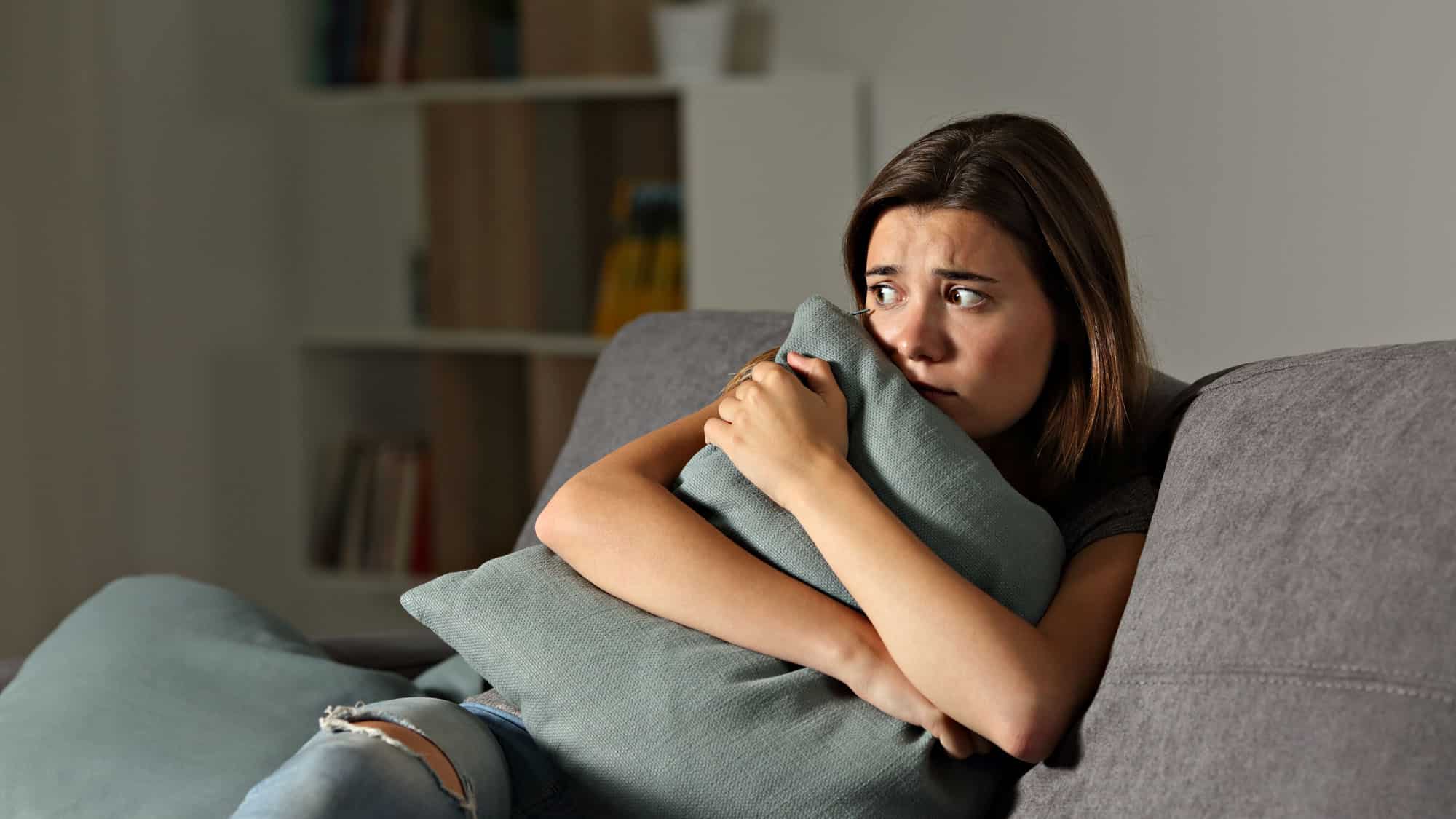 Anxious woman on couch clutching a pillow in worry