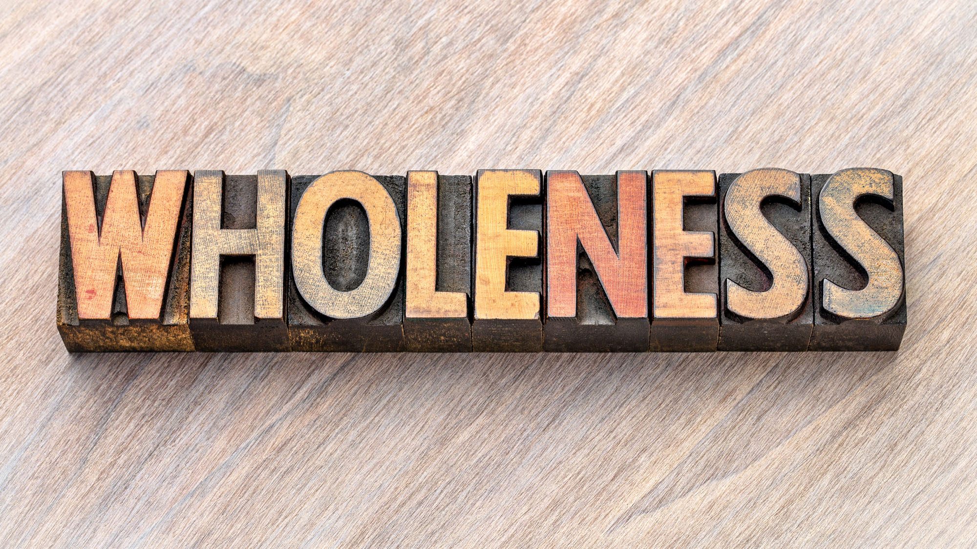 Vintage letterpress blocks spelling 'Wholeness' on wooden background