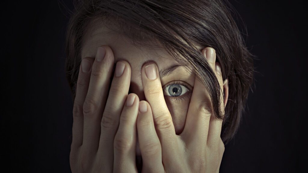 Person peering through hands covering face, showing one eye