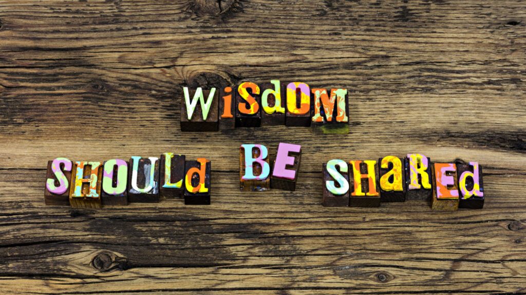 Colourful block letters spelling 'Wisdom Should Be Shared' on rustic wood